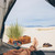 This is a tan brown leather duffle bag outside of a tent in the sand.